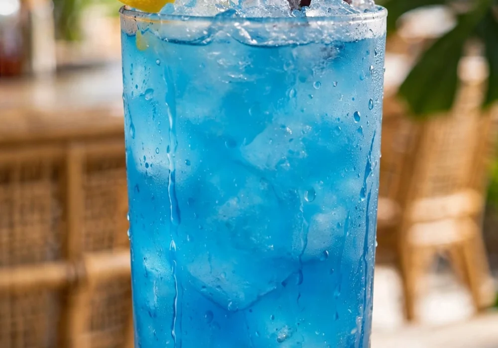 Tall glass of blue lagoon cocktail with ice, lemon twist, and turquoise color